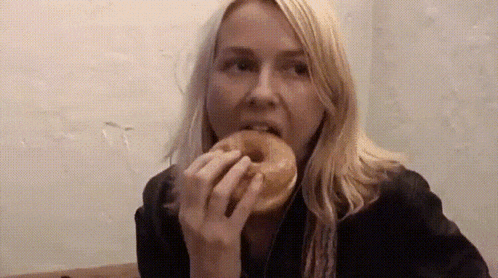 a woman is eating a donut in front of a white wall