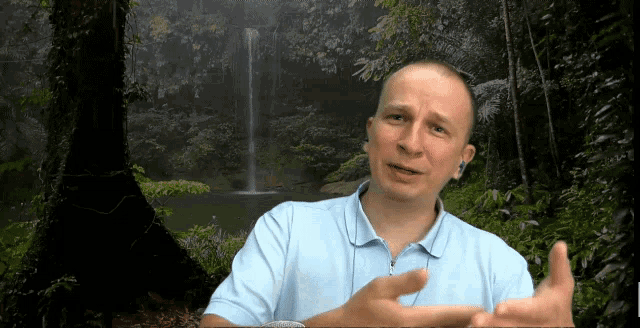 a man talking in front of a waterfall in the jungle