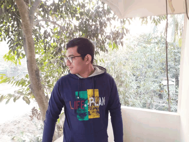 a man wearing a life plan sweatshirt stands in front of trees