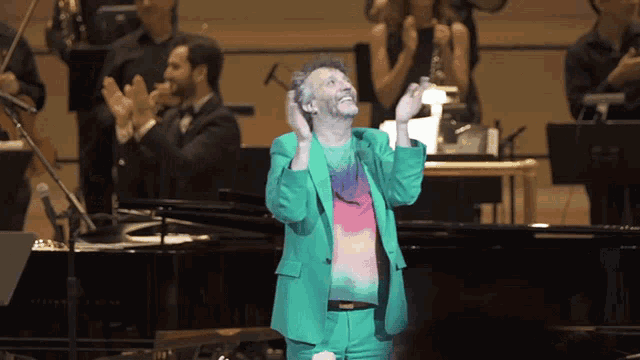 a man in a green suit stands on a stage with his hands in the air