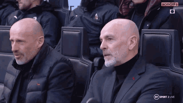 two bald men are sitting in a stadium with a bt sport 2 live advertisement in the corner