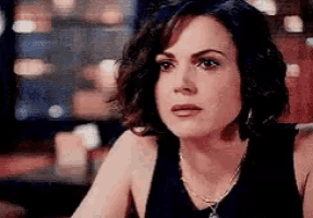 a woman is sitting at a table with a necklace on her neck and looking at the camera .