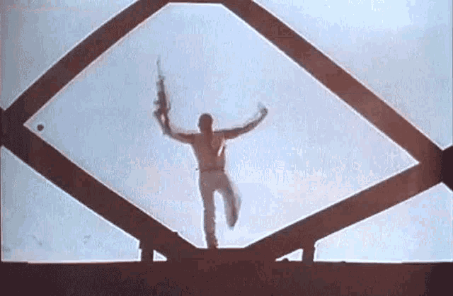 a man is jumping off a bridge while holding a gun in his hand .