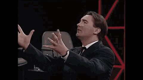 a man in a suit and tie is sitting in front of a microphone and talking into it .