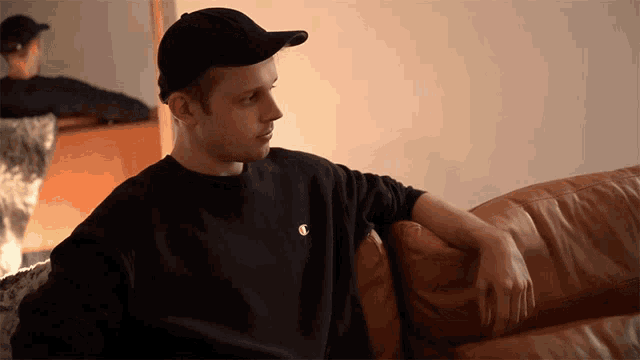 a man wearing a black champion sweatshirt sits on a brown couch