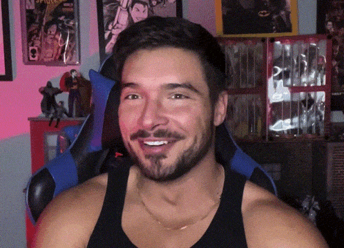a man with a beard wearing a black tank top is smiling in front of a spider-man poster