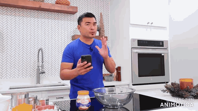 a man in a blue shirt is holding a cell phone in front of a bowl of food