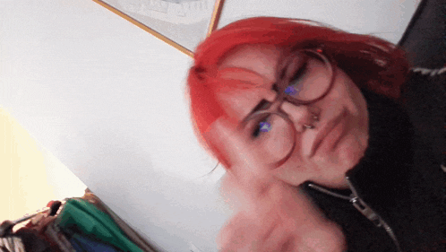 a woman with red hair and glasses making a funny face