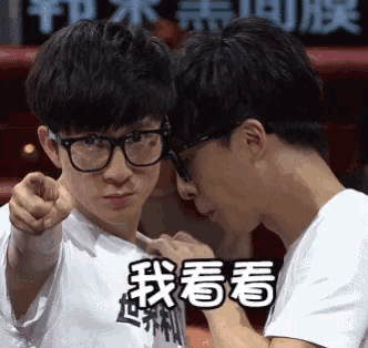 a man wearing glasses is pointing at another man with chinese writing on his shirt .