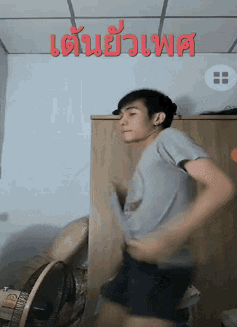 a man in a grey shirt is dancing in front of a sign that says ' เต้น '