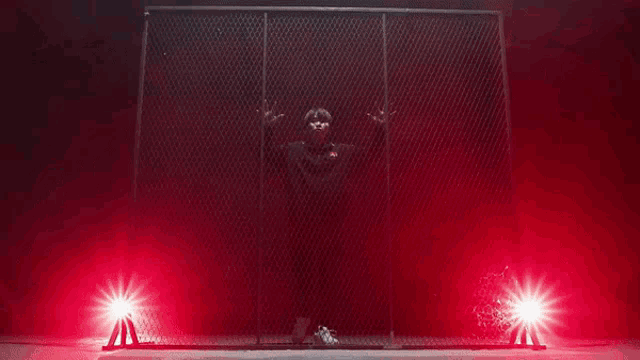 a man in a black jacket stands in a dark room with red lights behind him