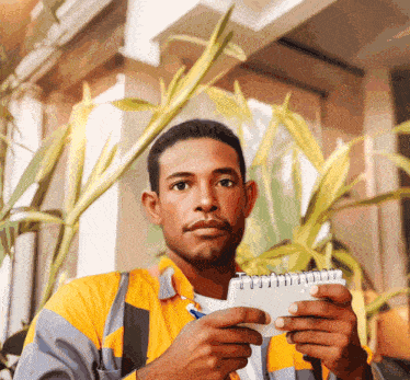 a man in a yellow and grey jacket is holding a notebook and a pen