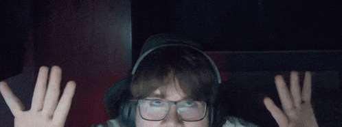 a man wearing glasses and headphones is making a funny face with his hands in the air .