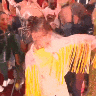 a woman wearing a yellow fringed jacket is dancing in a crowd .