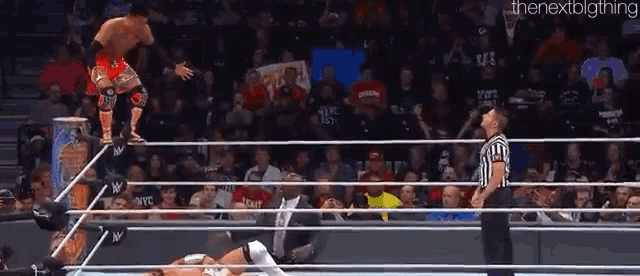 a wrestler is jumping over the ropes while a referee watches