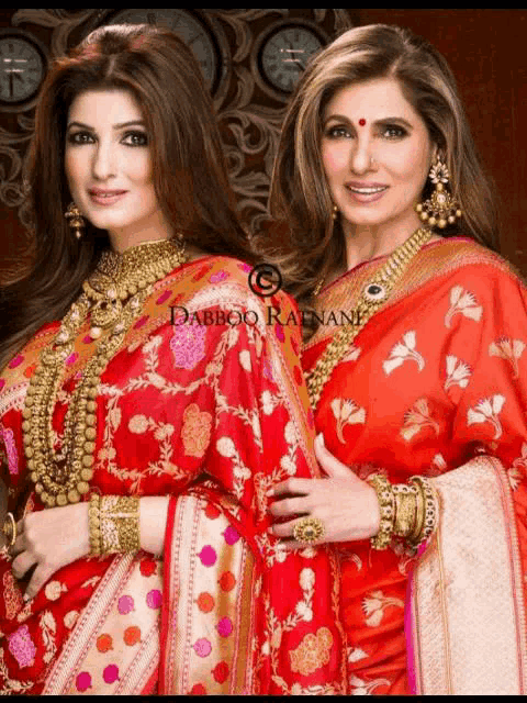 two women wearing red dresses and gold jewelry are standing next to each other in front of a sign that says dabboo radnani