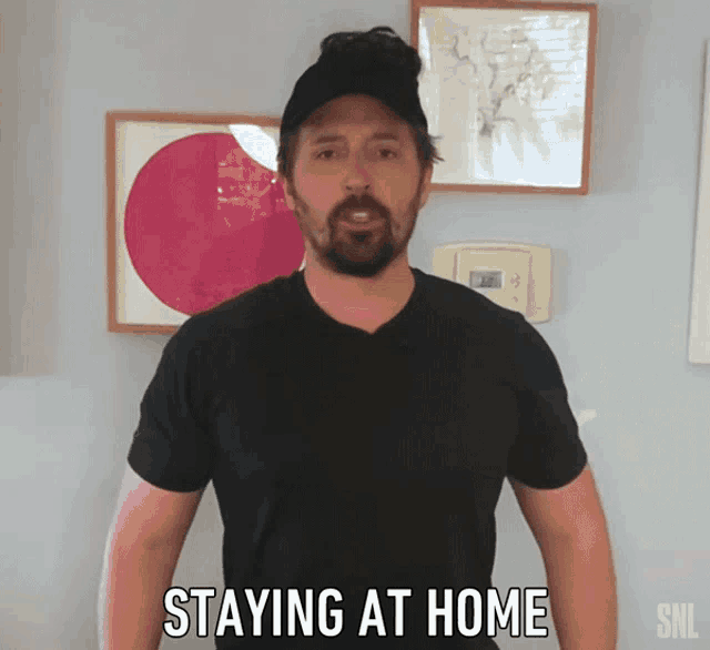 a man in a black shirt is standing in front of a thermostat that says staying at home