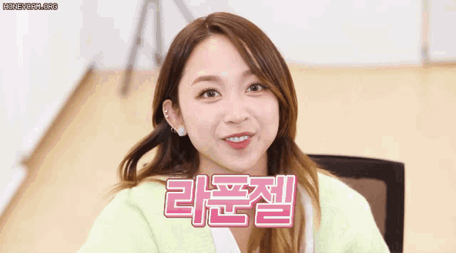 a woman in a green sweater is smiling in front of a sign that says ' korean ' on it