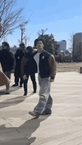 a man in a black jacket is walking down a sidewalk with other people .
