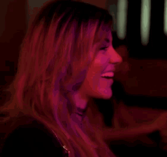 a woman is laughing with her eyes closed in a dark room .