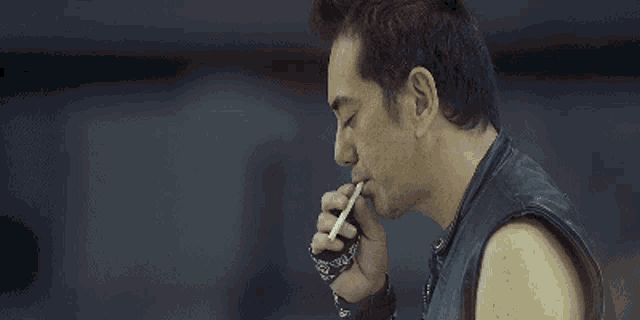 a man is smoking a cigarette while wearing a leather vest