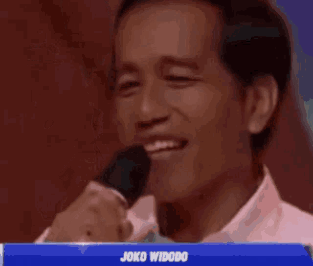 a man in a white shirt is singing into a microphone and smiling .