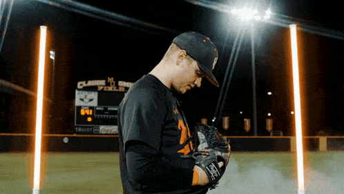 a baseball player stands in front of a scoreboard that says claude smith field
