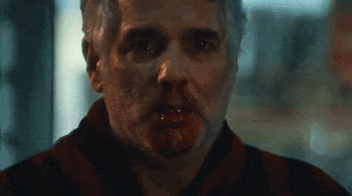 a man with blood coming out of his mouth looks at the camera
