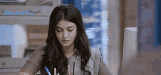a woman is sitting at a desk with a pen in her hand and the word pichukka is visible in the corner