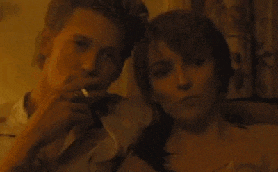 a man is smoking a cigarette while sitting next to a woman on a couch .