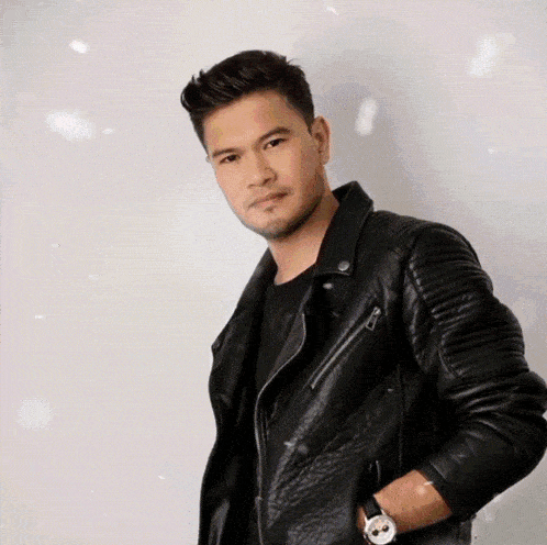 a man wearing a black leather jacket and a watch looks at the camera