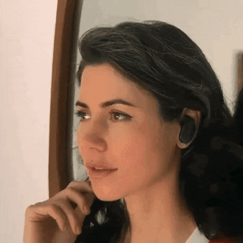a woman wearing a pair of earbuds looks at herself in a mirror