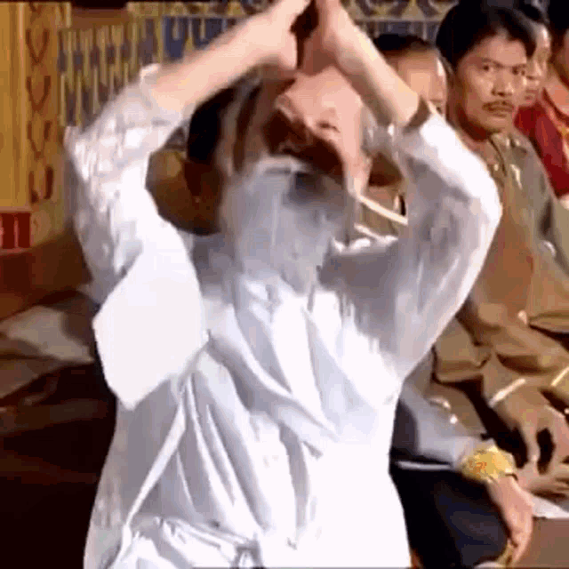 a man with a beard is dancing in front of a crowd of people in a room .