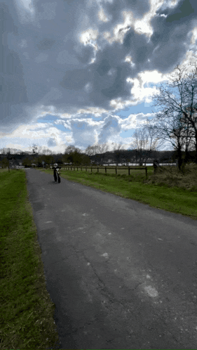 a person riding a bike down a road with a cloudy sky