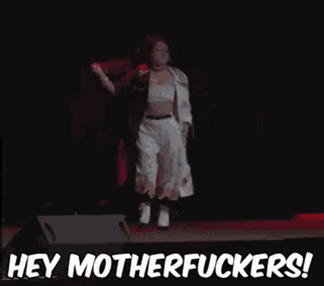 a woman is standing on a stage with the words hey motherfuckers behind her