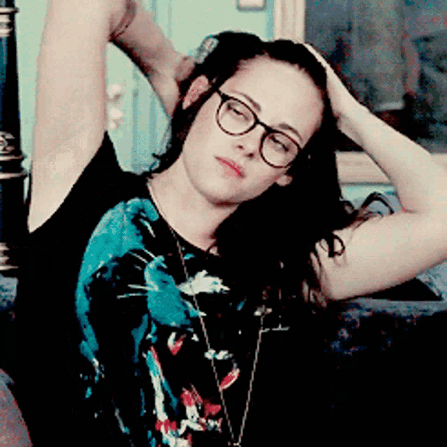 a woman wearing glasses holds her hand to her head while sitting on a couch