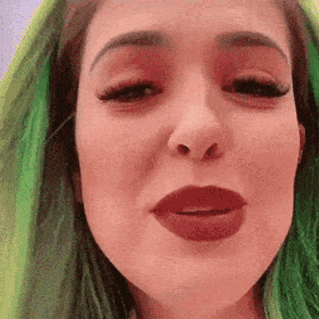 a close up of a woman 's face with green hair and red lipstick