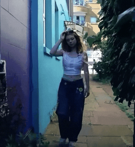 a woman walking down a sidewalk with a blue wall behind her
