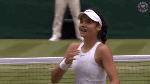 a woman in a white tank top and visor is playing tennis on a tennis court .