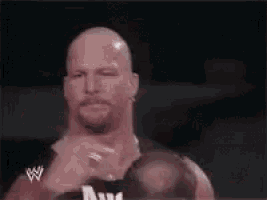 a bald man with a beard and a w logo on his shirt is making a funny face .