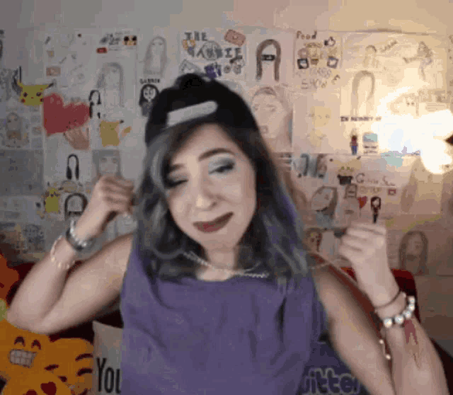 a woman in a purple tank top is standing in front of a wall with drawings on it