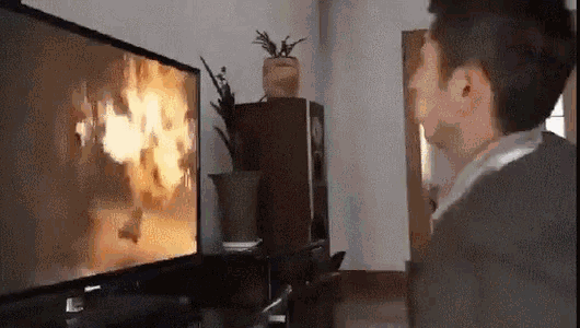 a man is standing in front of a television watching a fire .
