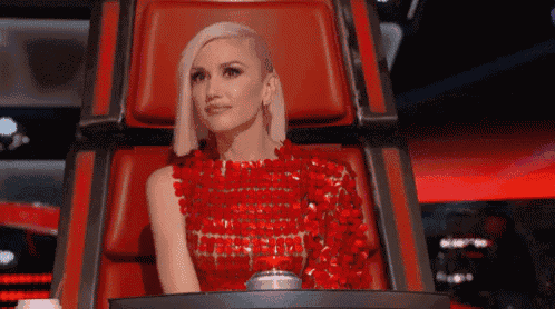 a woman in a red dress is sitting in a red chair on a stage .