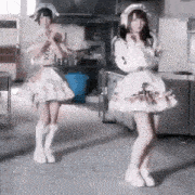 two women are dancing in a kitchen wearing dresses and hats .