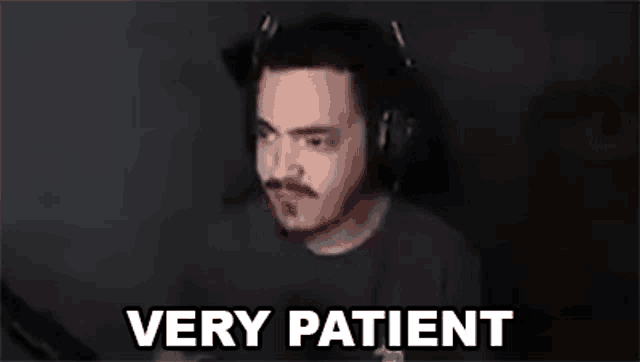 a man wearing headphones is sitting in front of a computer screen with the words `` very patient '' written on it .