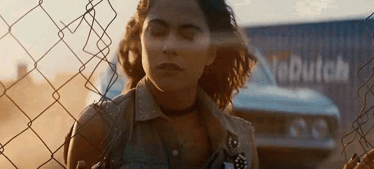 a woman is standing behind a chain link fence with a car in the background .