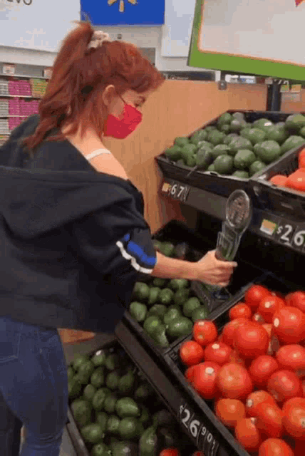a woman wearing a red mask is looking at tomatoes and avocados
