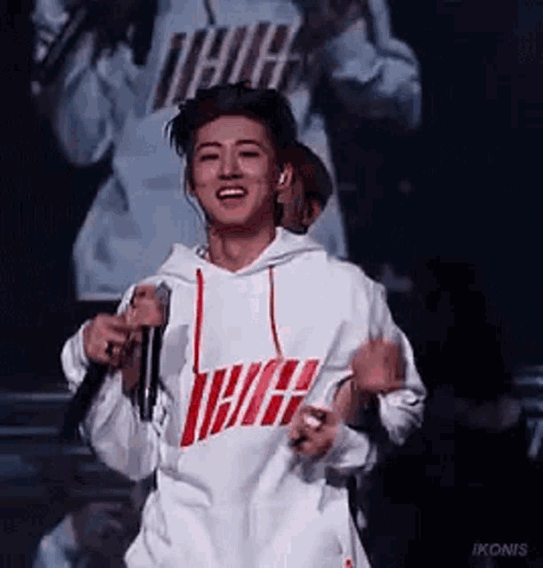 a young man in a white hoodie is holding a microphone on a stage and smiling .