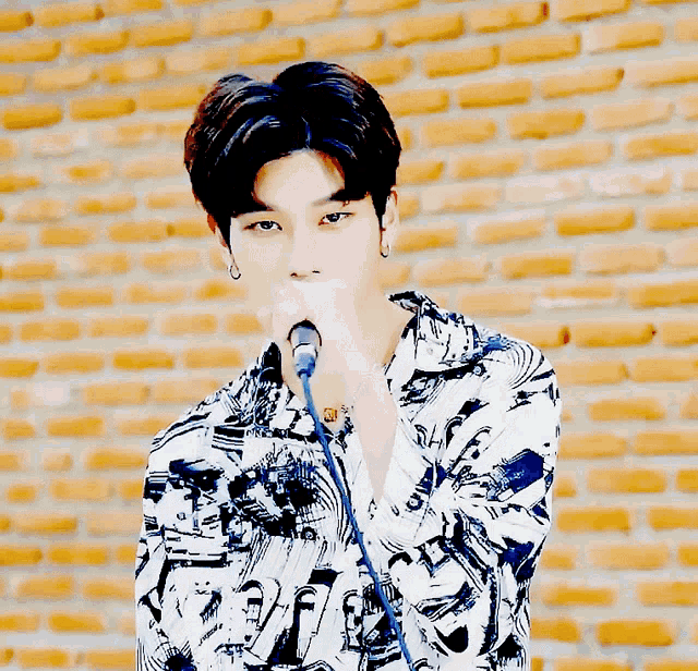 a young man singing into a microphone in front of a yellow brick wall