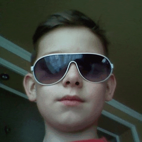 a young boy wearing sunglasses is looking at the camera and making a funny face .